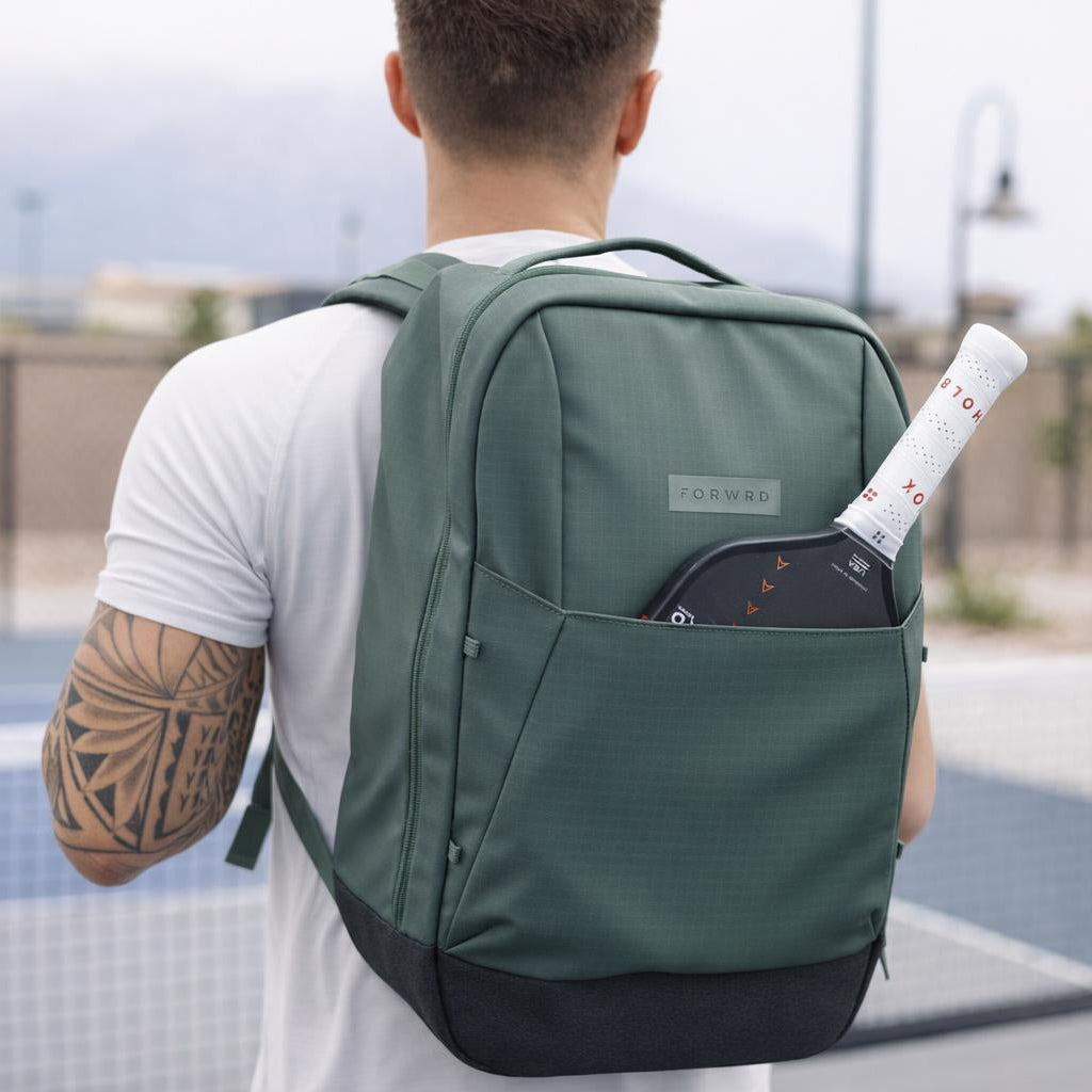 Person with a green backpack holding a tennis racket on a court