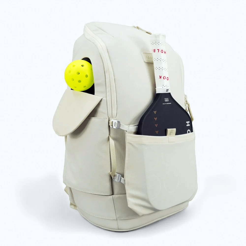 Beige backpack with a yellow ball and black device in front pocket on a white background