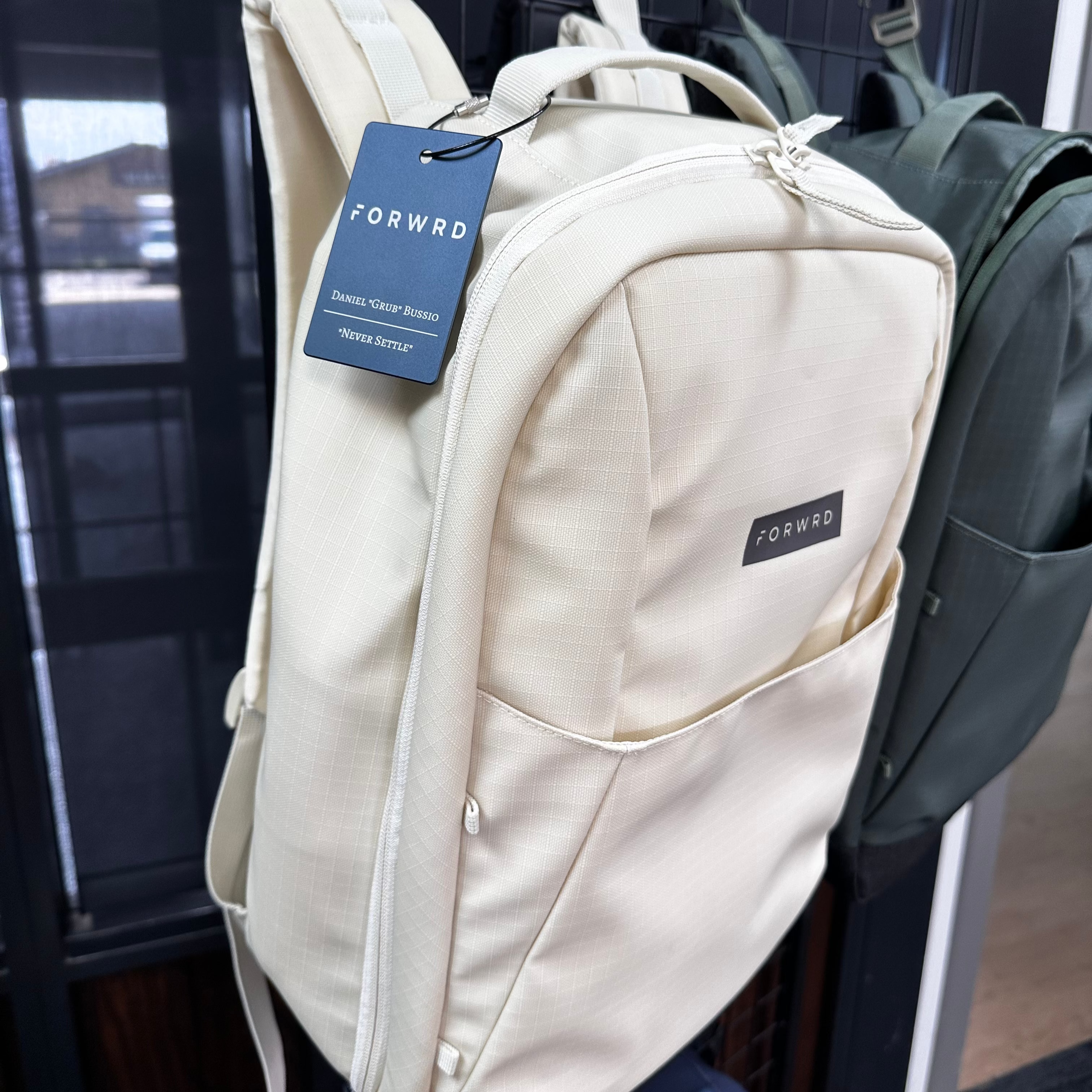 Beige backpack with a 'FORWD' tag on a rack.
