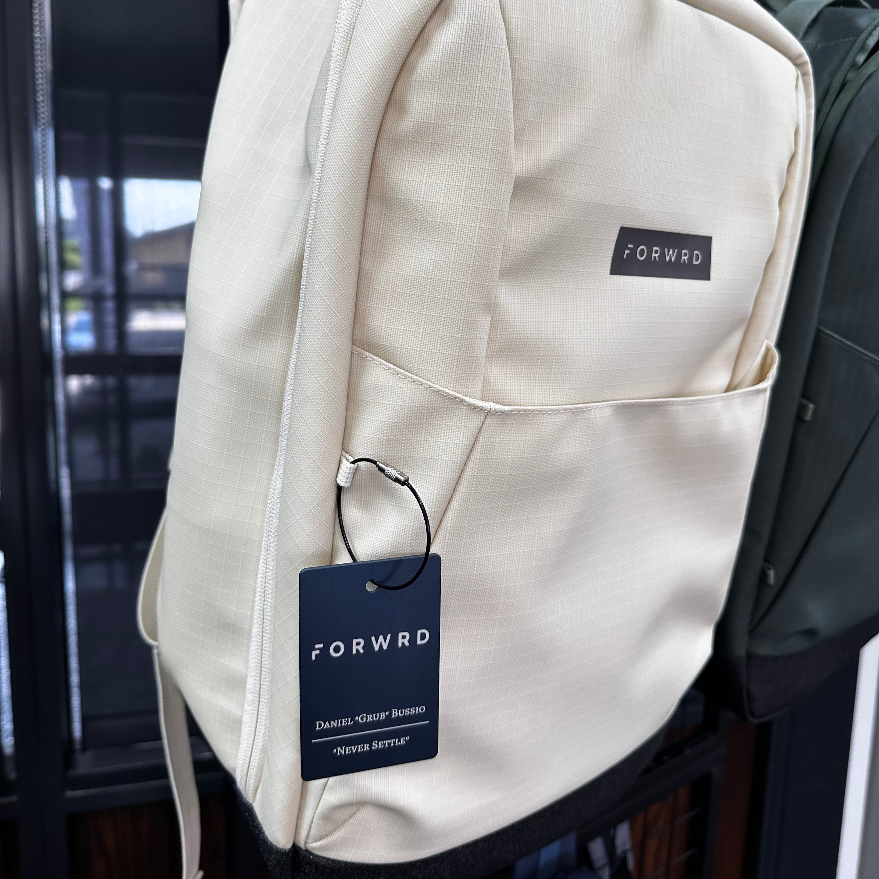 Beige backpack with a tag labeled 'FORWARD' on a dark background