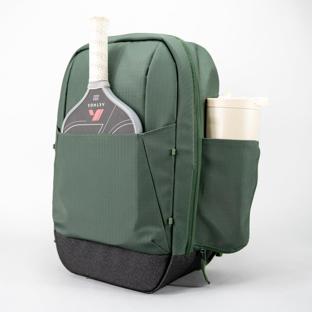Green FORWRD Court Ranger pickleball backpack with a Aethos pickleball paddle stored inside the integrated paddle sleeve front pocket and a beige Hydrojug water bottle in the side pocket, built with durable ripstop, coated nylon fabric.