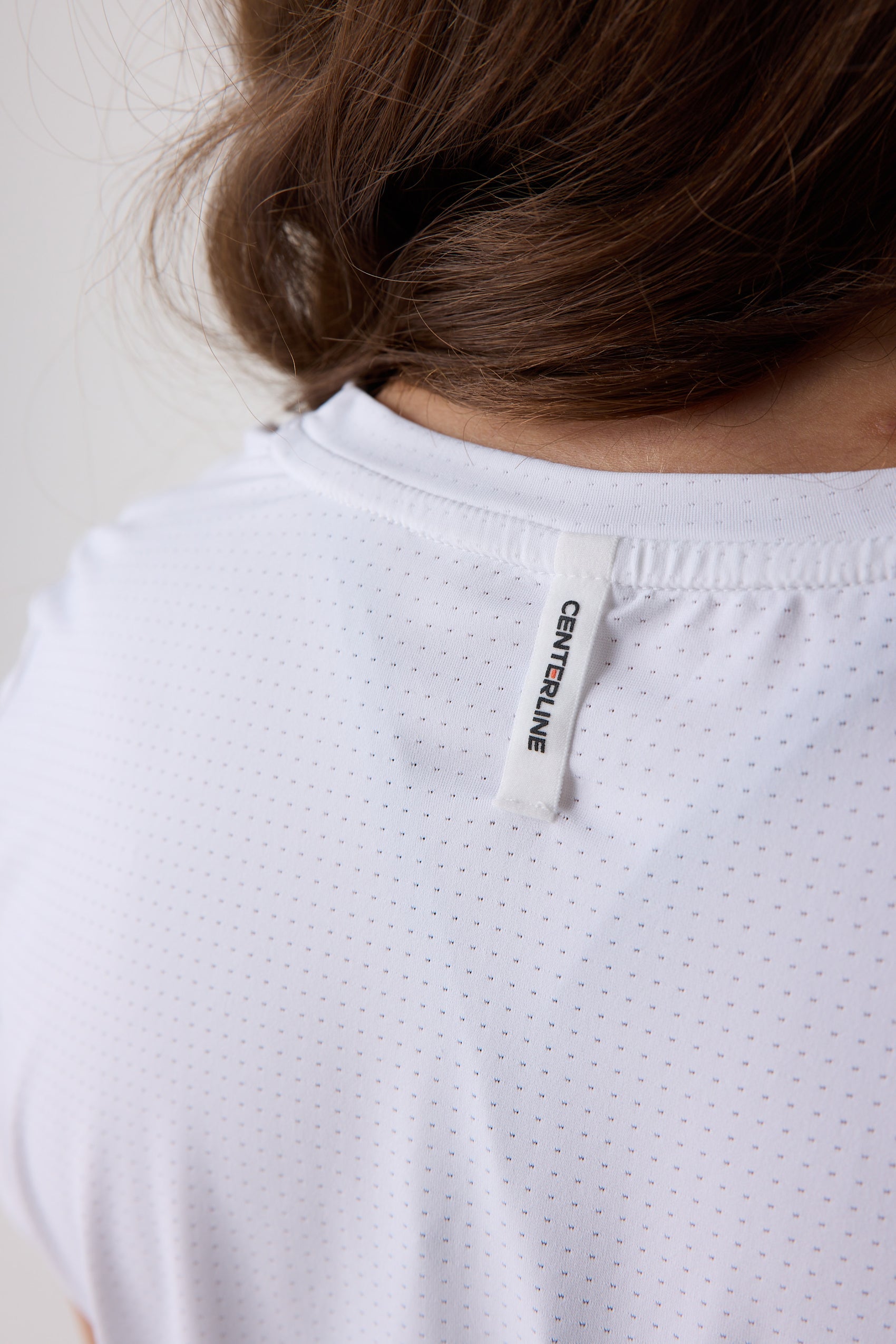 Close-up of a person wearing a white shirt with a brand label on a plain background