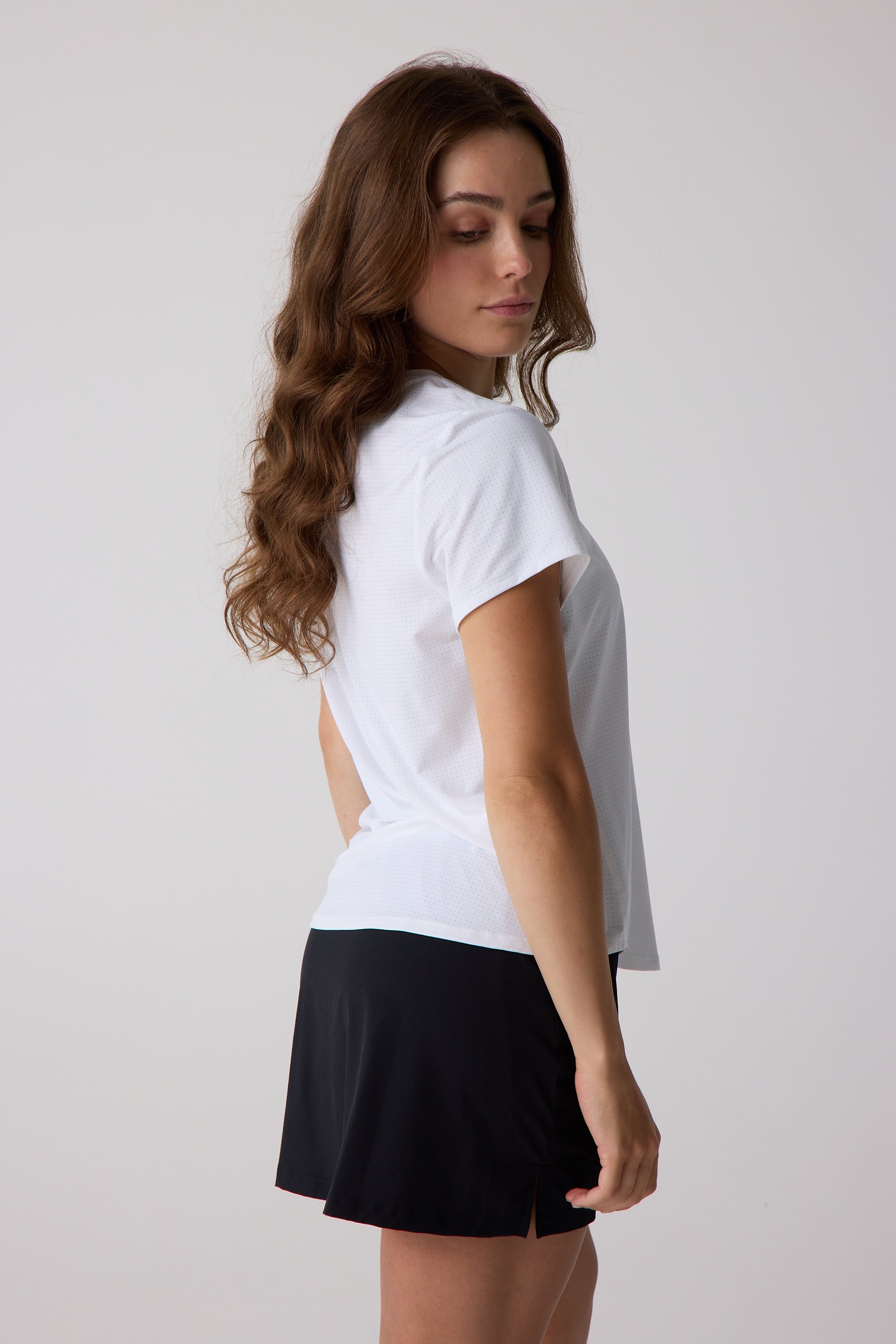 Woman wearing a white t-shirt with cut-out design and black shorts on a plain background