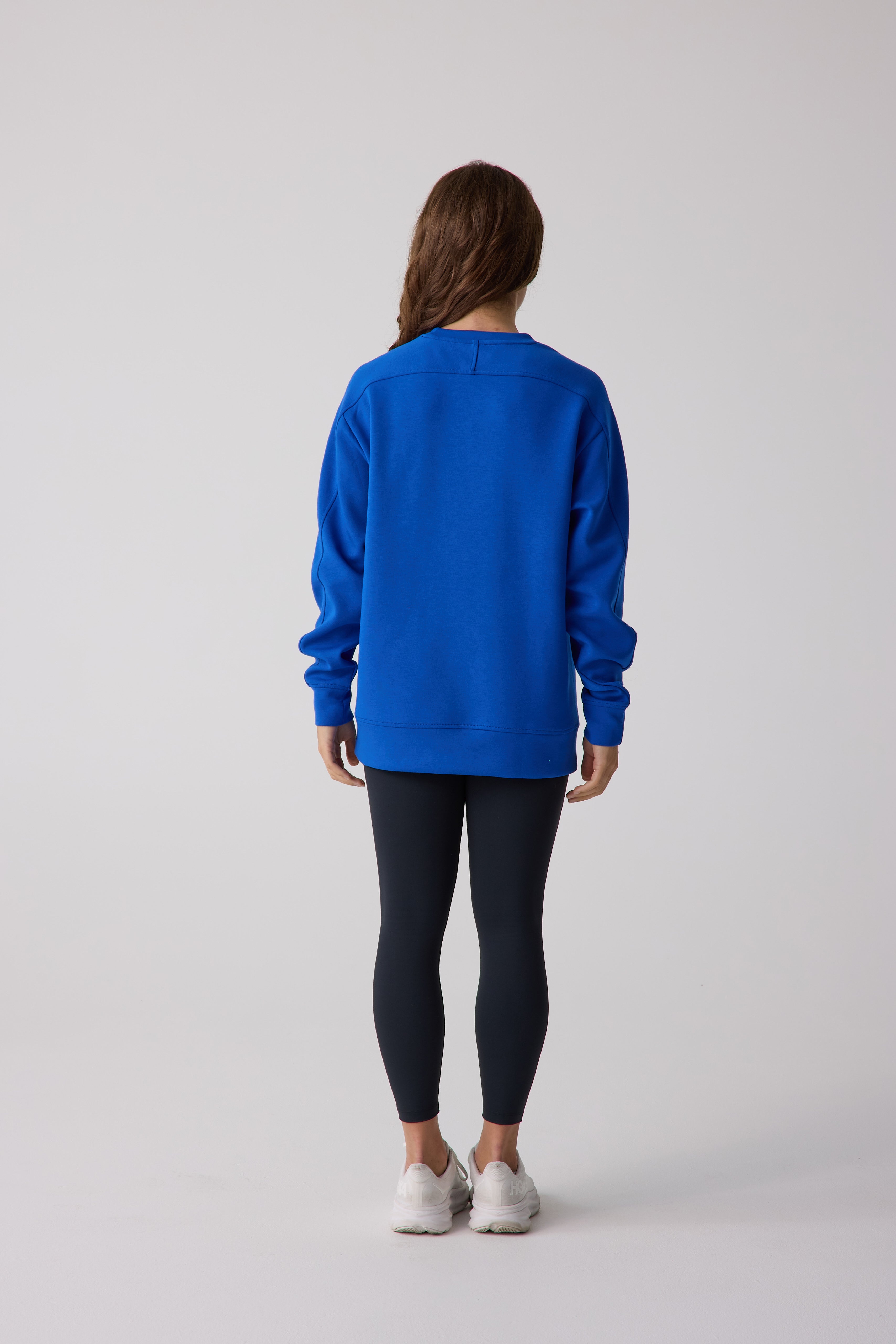 Person wearing a blue sweatshirt and black leggings on a white background