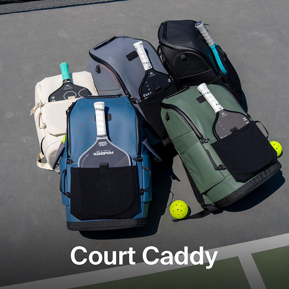 Five FORWRD Court Caddy pickleball bags in assorted colors on court surface with paddles inserted and balls nearby