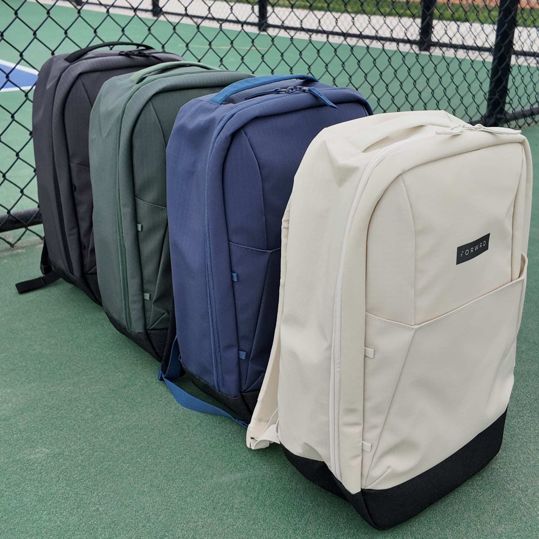 Four backpacks in different colors arranged on a green surface.