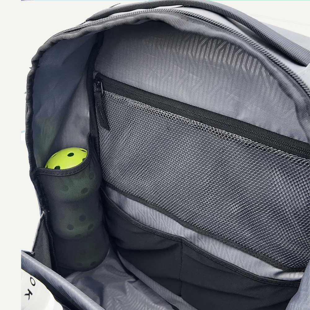 Gray backpack with a compartment containing a green pickleball paddle and ball.