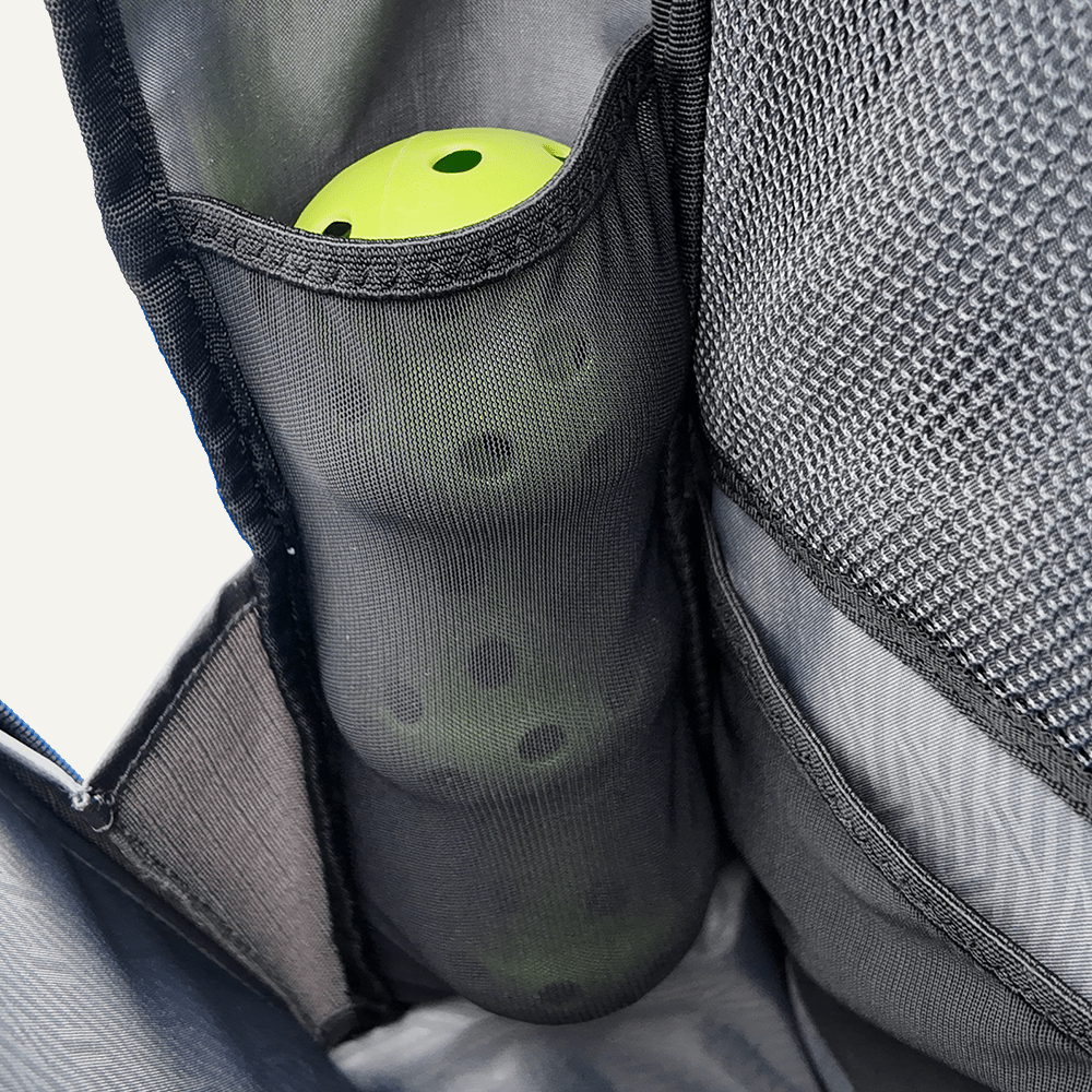 Close-up of a gray mesh bag with a green pickle inside, attached to a gray backpack.