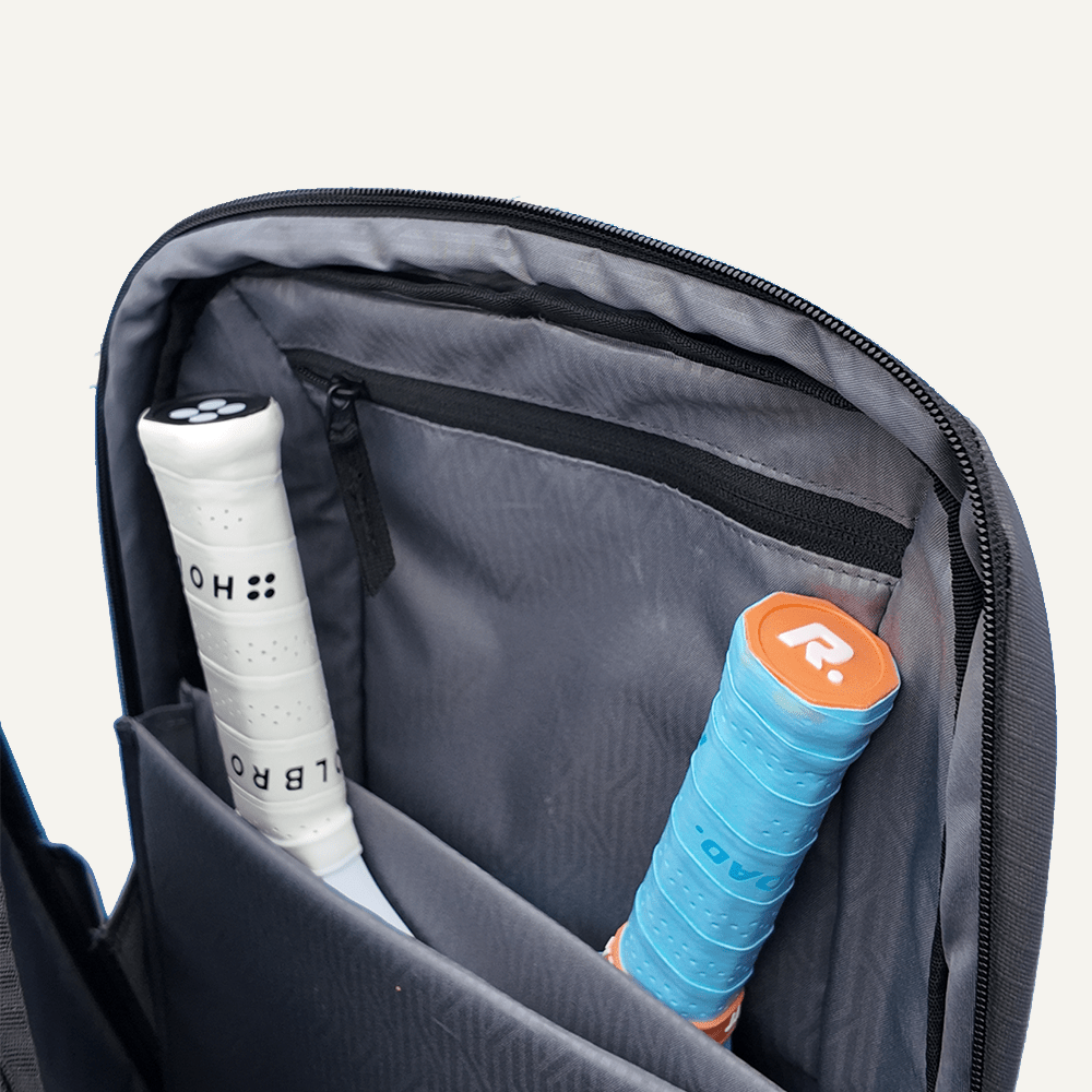 Gray backpack with pickleball accessories including a white racket and blue and orange racket cover.