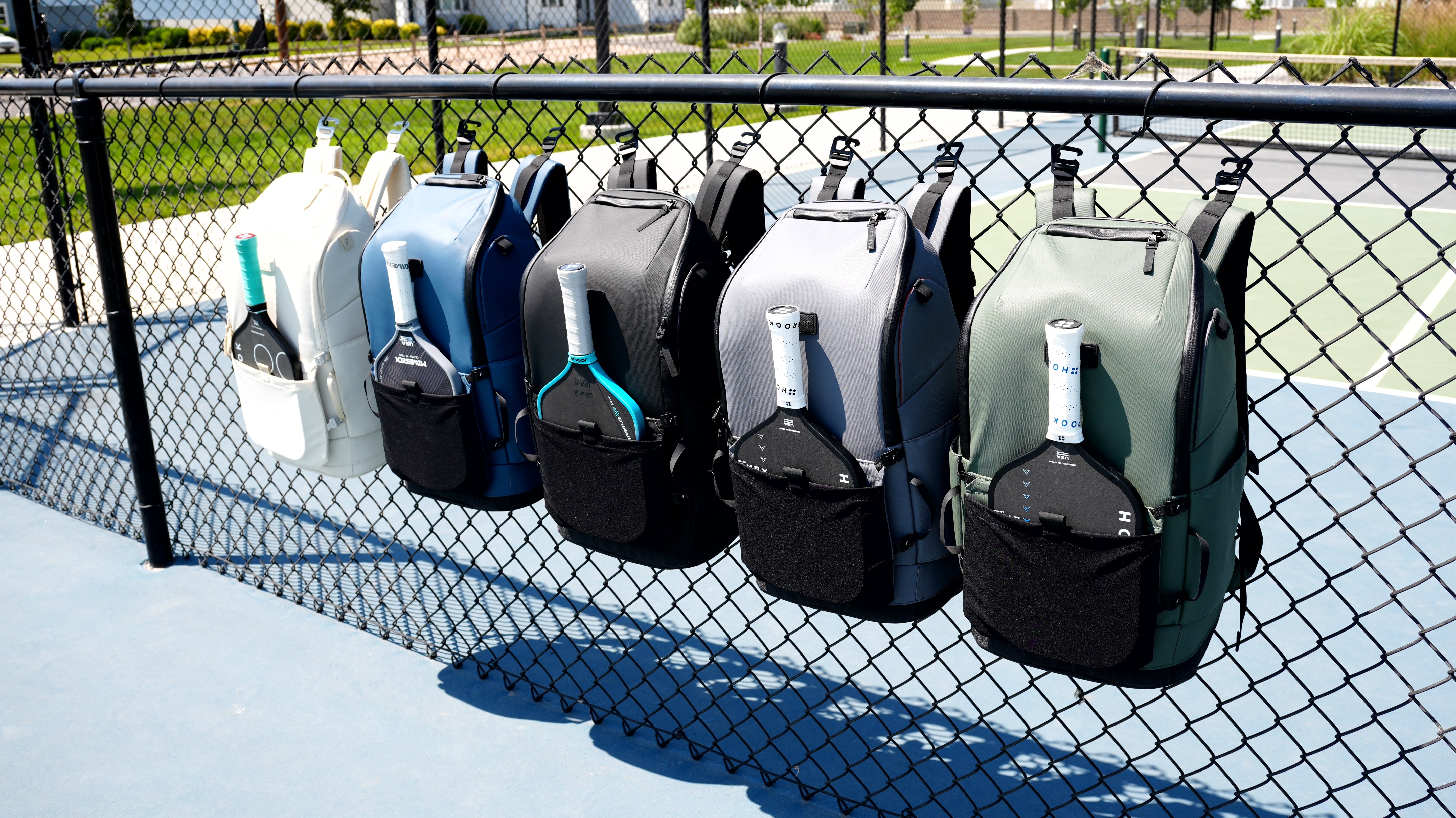 FORWRD pickleball bags in six colors hanging on a court fence with paddles inserted, premium gear display
