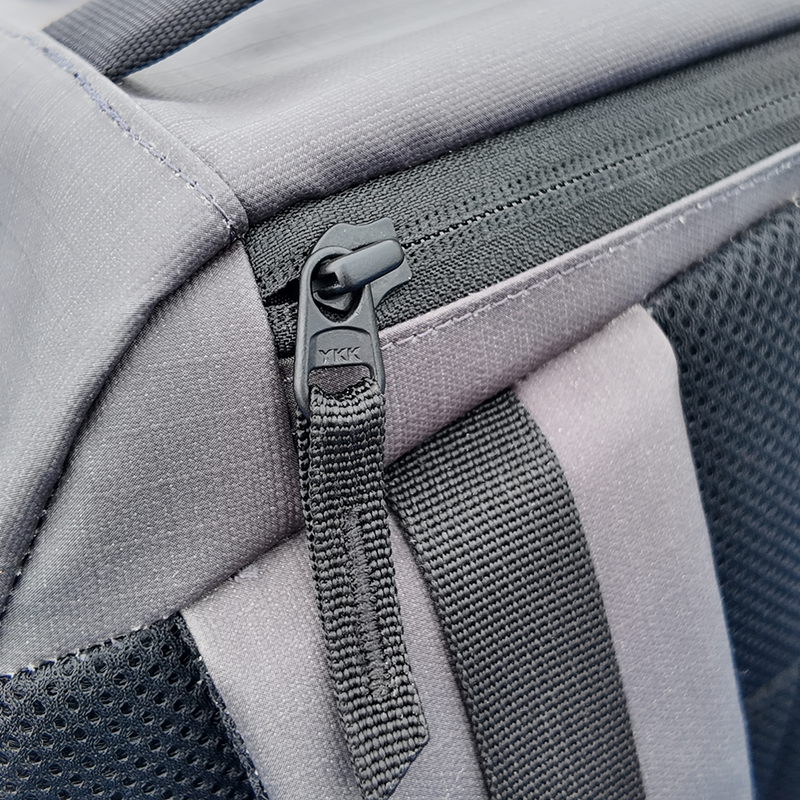 Close-up of a grey backpack zipper with black pull tab.