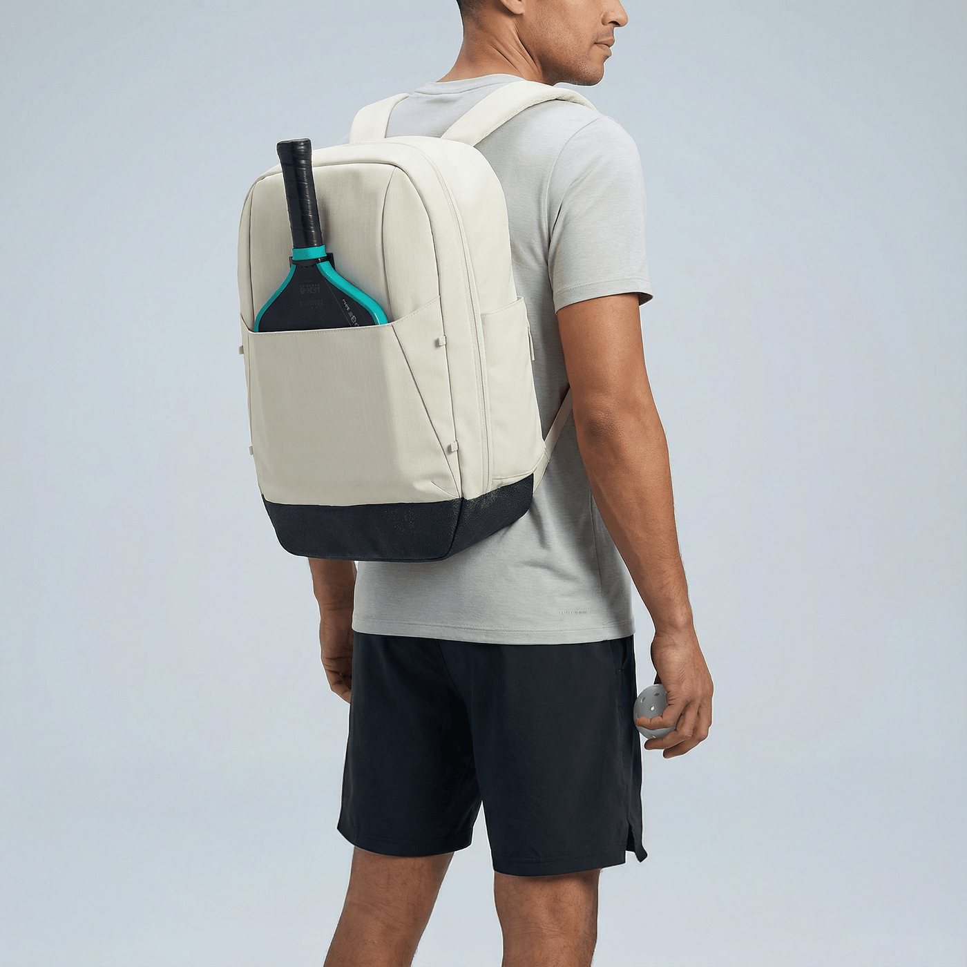 Man wearing a beige backpack with a paddle in a pocket on a light gray background