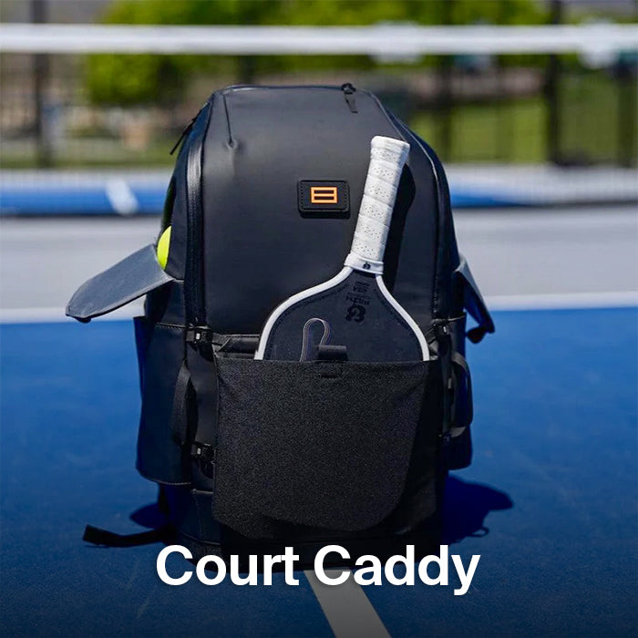 Black Court Caddy pickleball backpack on a bright blue court, featuring a white-gripped paddle in the front pocket—highlighting organized on-court gear storage.