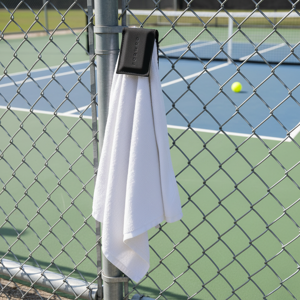 White towel hanging on a chain-link fence with a tennis court in the background